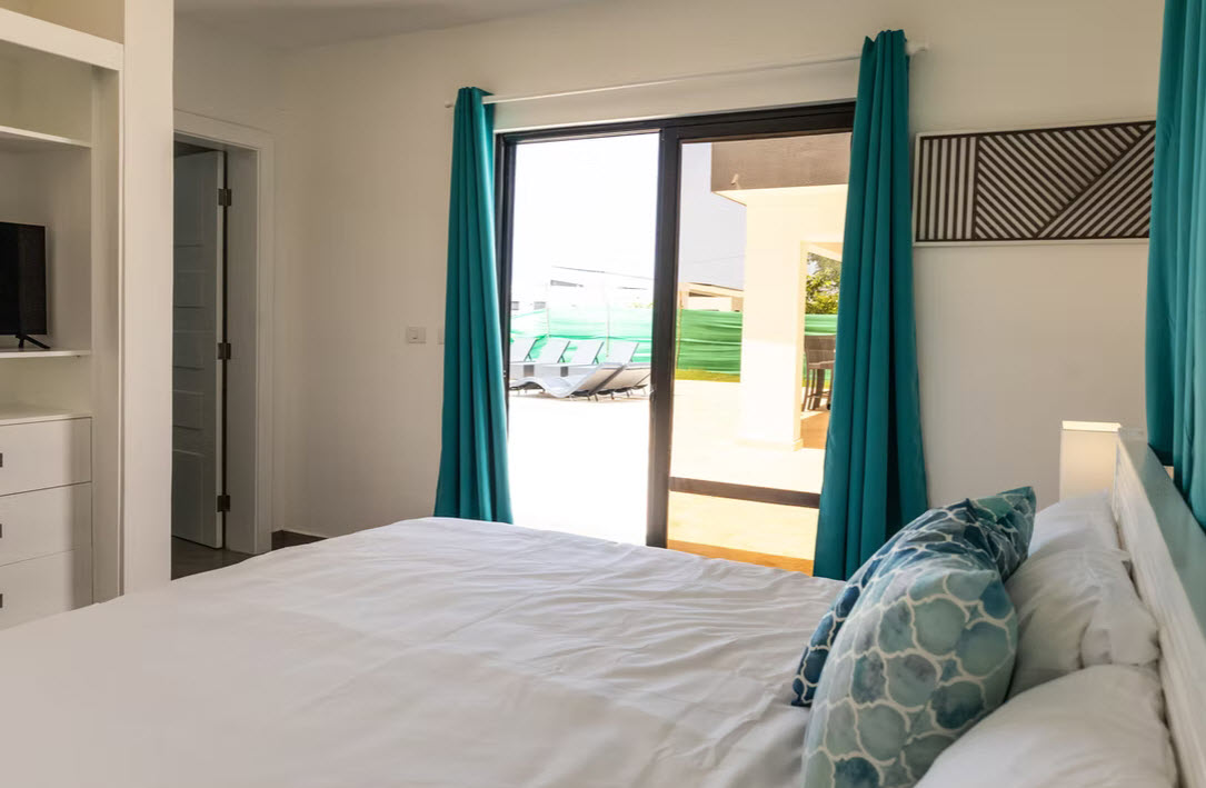 Bedroom with white bedding, teal curtains, and view of a pool