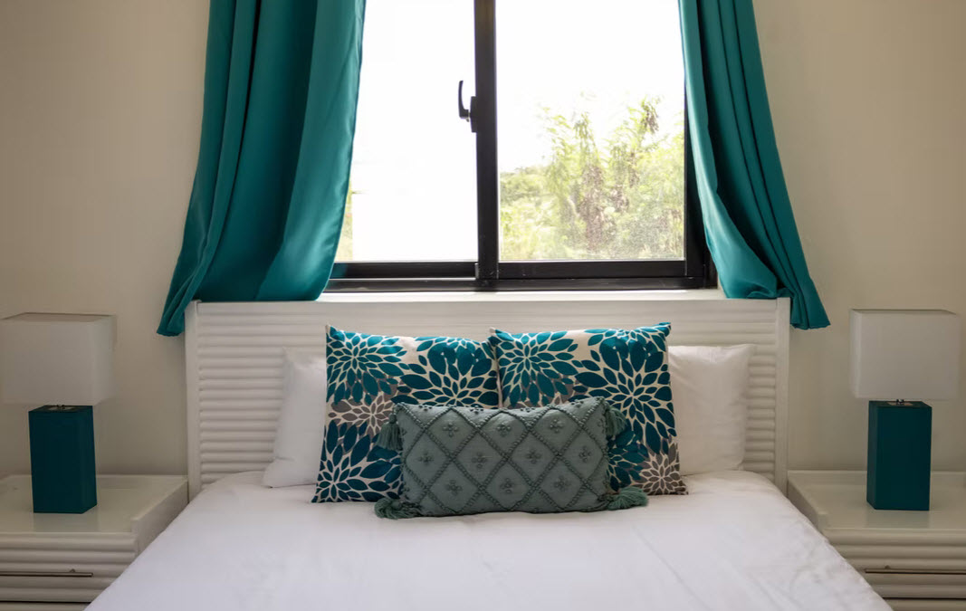 Bedroom with white bed, teal curtains, and decorative pillows