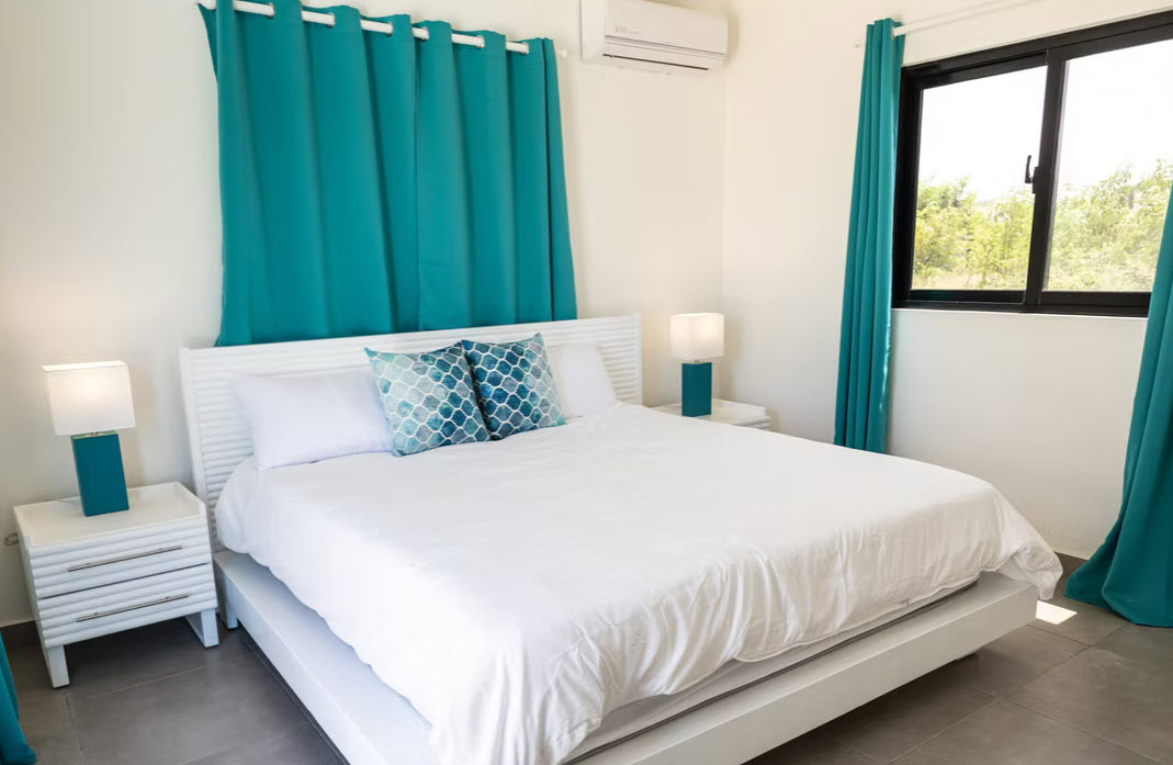 Coastal bedroom with white bed, teal curtains, and ocean view from window