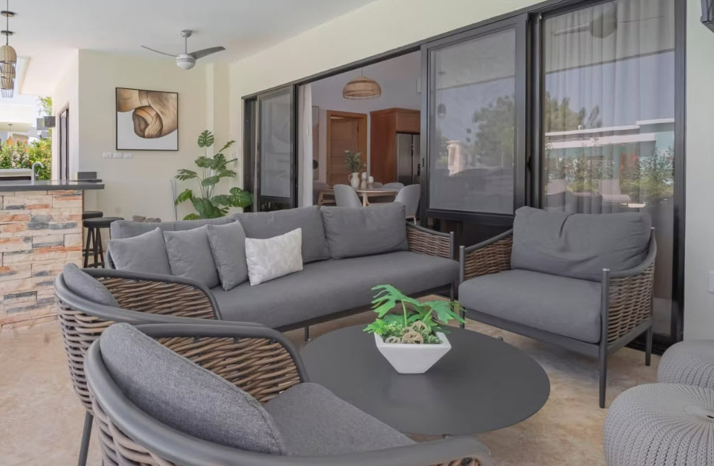 Modern outdoor living room with gray sofa, wicker chairs, and coffee table.