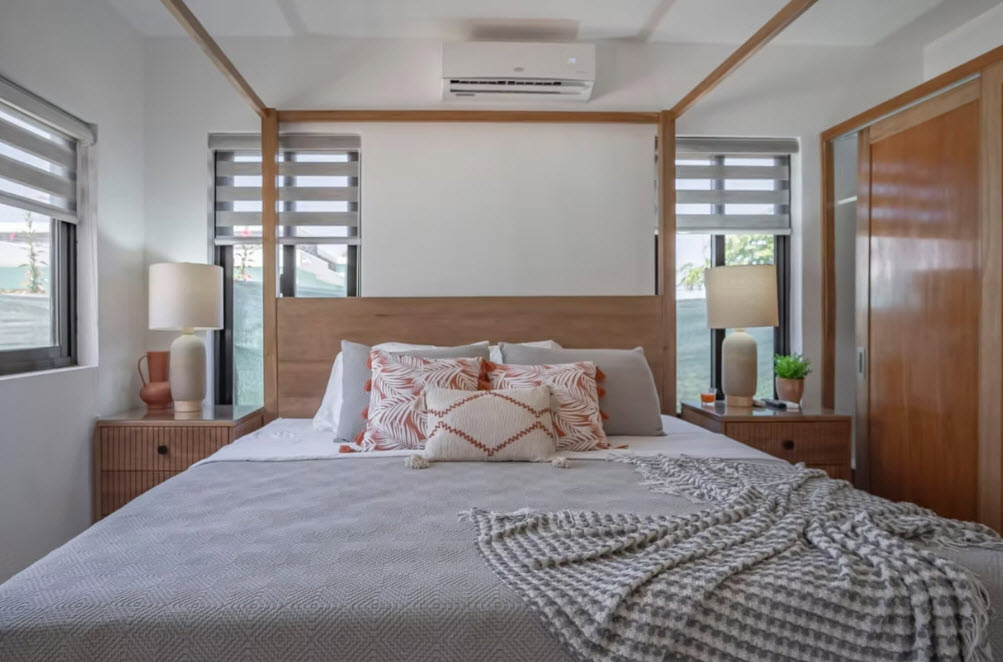 Modern bedroom with a wooden four-poster bed, patterned pillows, and bedside lamps