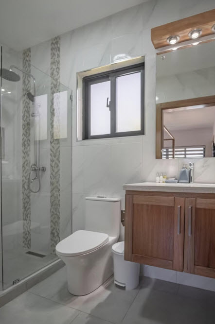Modern bathroom with a wooden vanity, glass shower, and white toilet.
