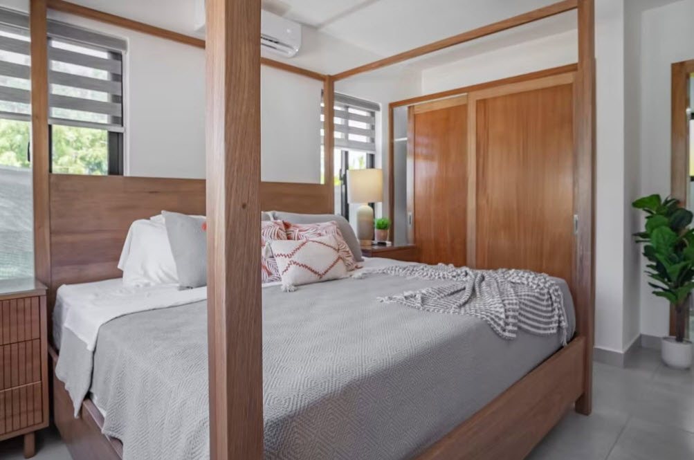 Modern wood canopy bed with grey bedding and decorative pillows in a bright bedroom