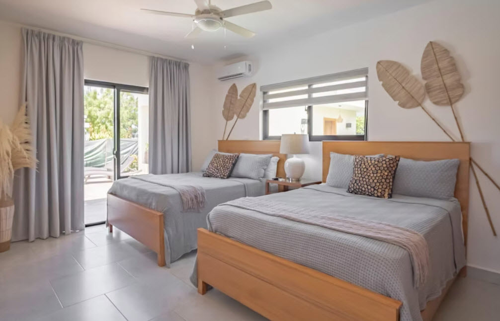 Two queen beds in a bright, modern bedroom with tropical decor