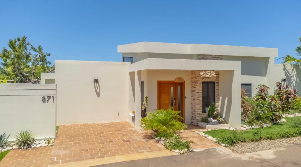 Modern beige house with a wooden door, stone accents, and lush landscaping