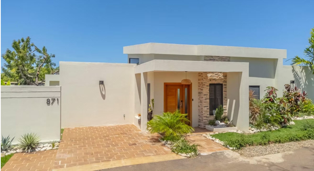 Modern beige house with a wooden door, stone accents, and lush landscaping