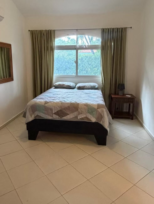 Cozy bedroom with a queen bed, green curtains, and a large window overlooking lush greenery.