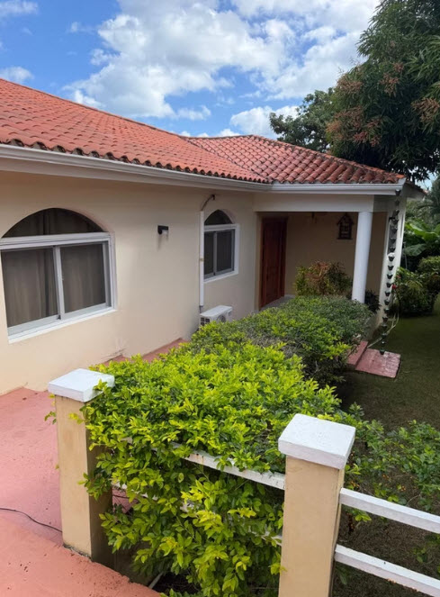 Tiled roof home with lush green landscaping and white pillars.