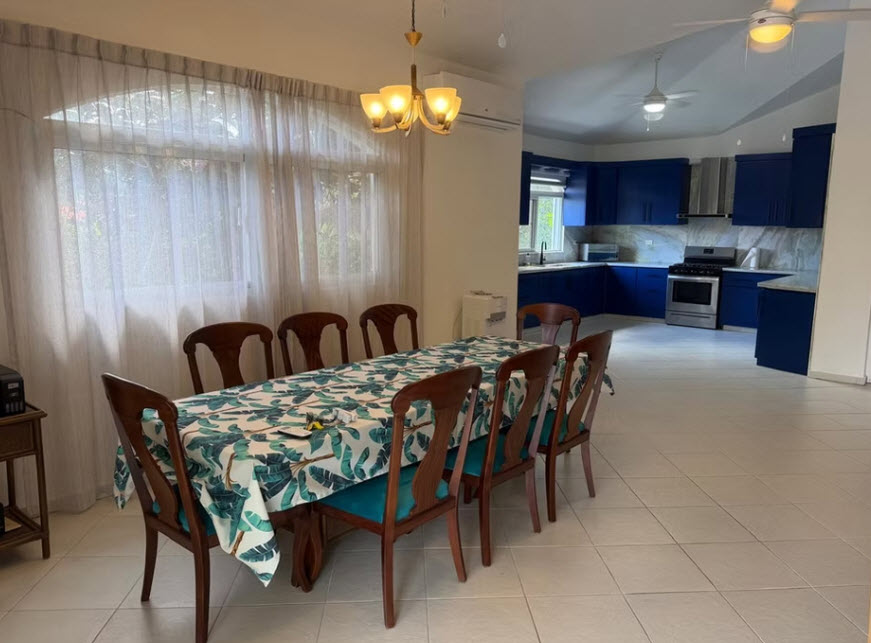 Elegant dining room with a tropical-print tablecloth and a modern blue kitchen.
