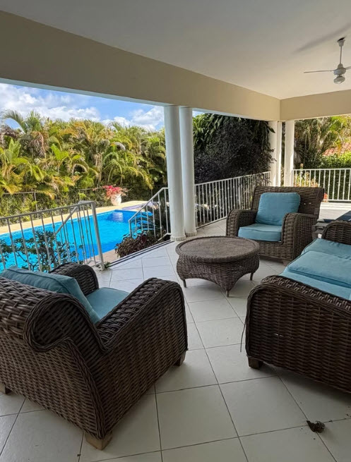 Wicker patio furniture and pool with lush tropical foliage