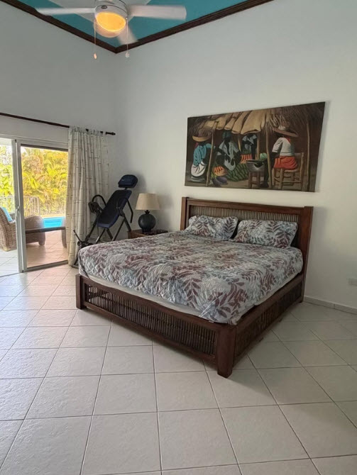 Tropical master bedroom with a king-size bed, island art, and pool view.
