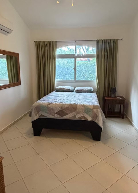 Cozy bedroom with a queen bed, large window, and tiled floor