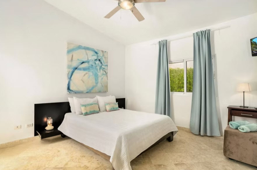 Modern bedroom with a queen bed, abstract art, and blue curtains.
