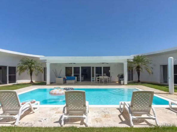 Modern villa with swimming pool, lounge chairs, and palm trees under a clear blue sky.