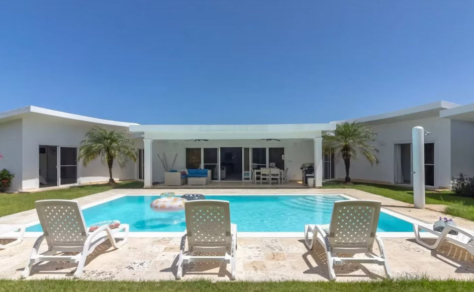 Modern villa with swimming pool, lounge chairs, and palm trees under a clear blue sky.