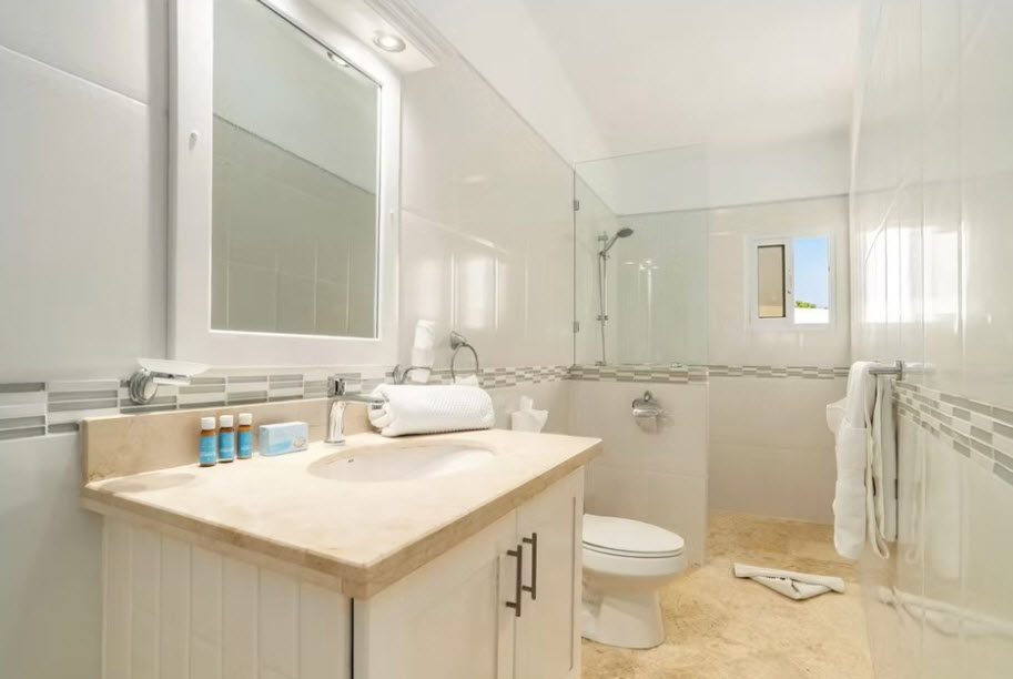 Bright, modern hotel bathroom with white tiles, marble vanity, and glass shower.