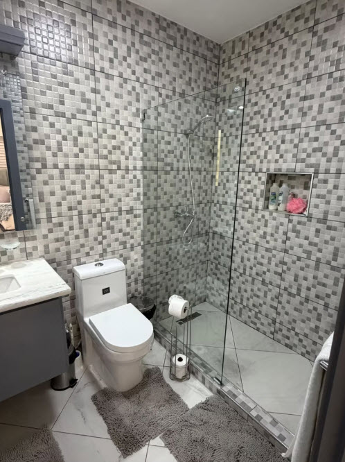 Modern bathroom with mosaic tile, glass shower, toilet, and vanity