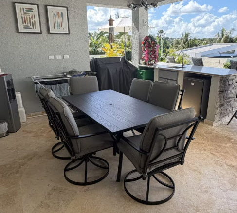 Outdoor patio dining set with six chairs and a large table, under a covered area.