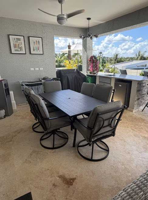 Outdoor patio dining set with six chairs and a large table, under a covered area.