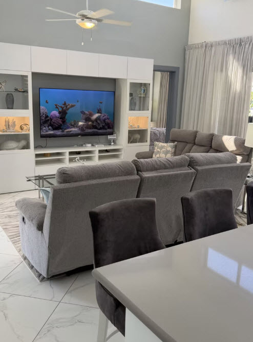 Modern living room with large TV displaying aquarium, comfortable recliners, and built-in shelving.