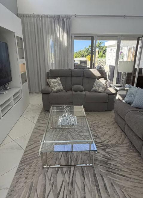 Modern living room with gray reclining sofa, glass coffee table, and large windows