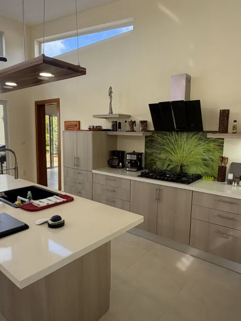 Modern kitchen with light wood cabinets, a large island, and a vibrant green grass backsplash.