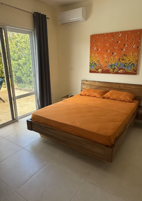 Modern wood bed with orange bedding in a tropical bedroom with sliding glass door