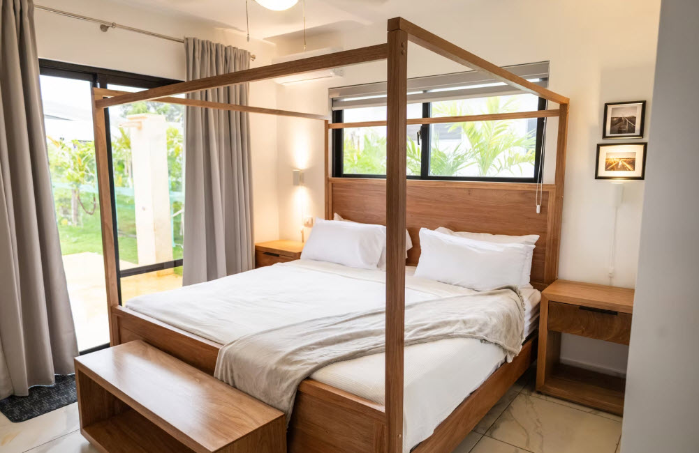 Modern four-poster wooden bed with white linens in a bright bedroom