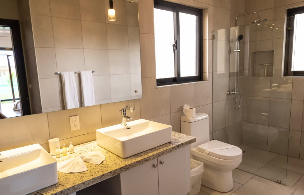 Modern hotel bathroom with double vanity, glass shower, and clean white toilet.