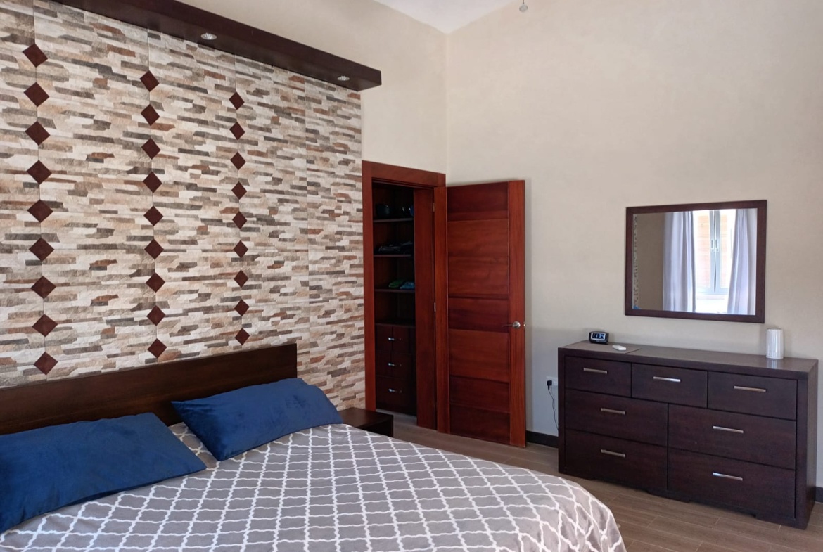 Modern bedroom with patterned accent wall, wooden closet, and dresser with mirror.