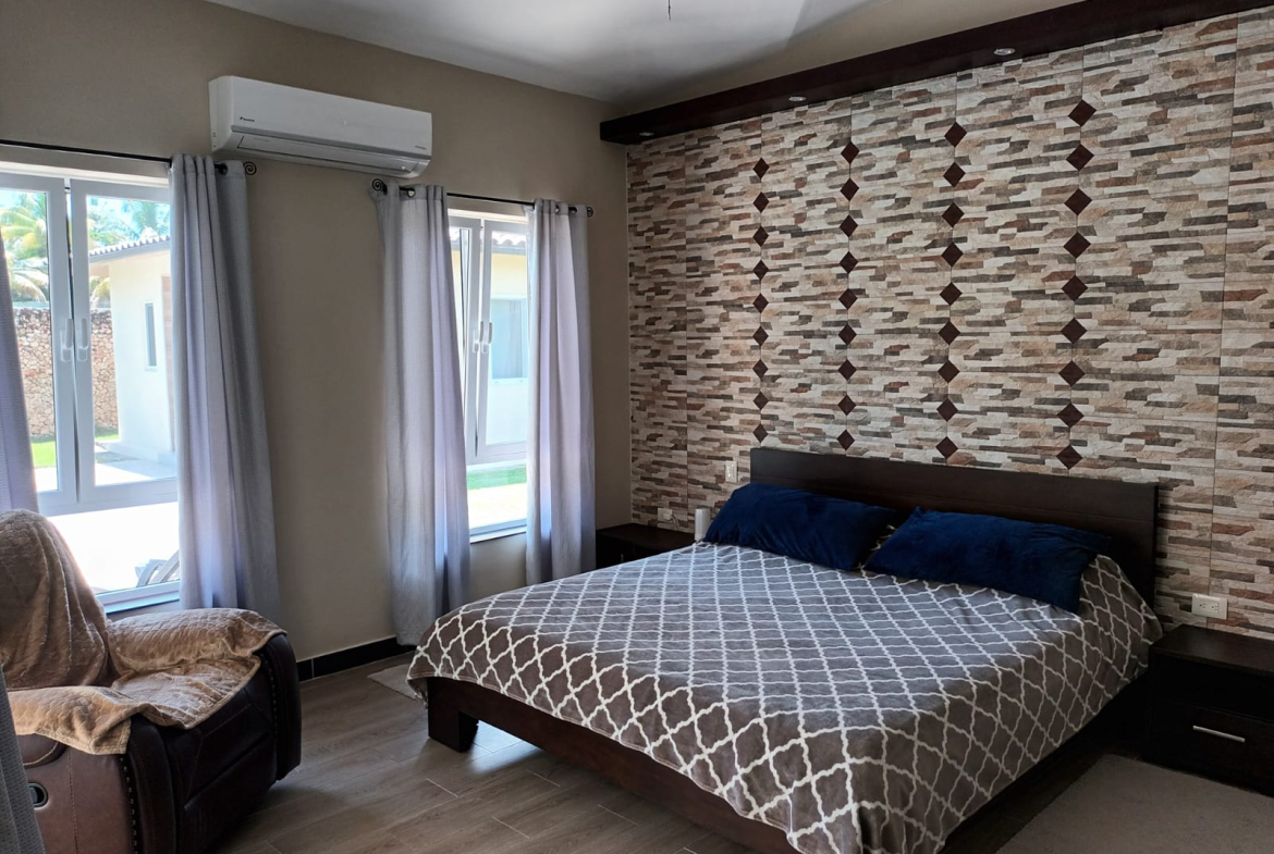 Cozy bedroom with patterned bedding, textured accent wall, and large windows.