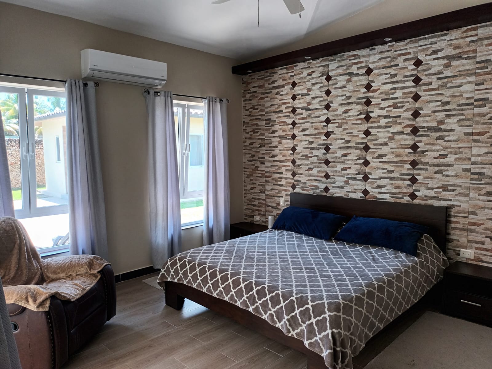 Cozy bedroom with patterned bedding, textured accent wall, and large windows.