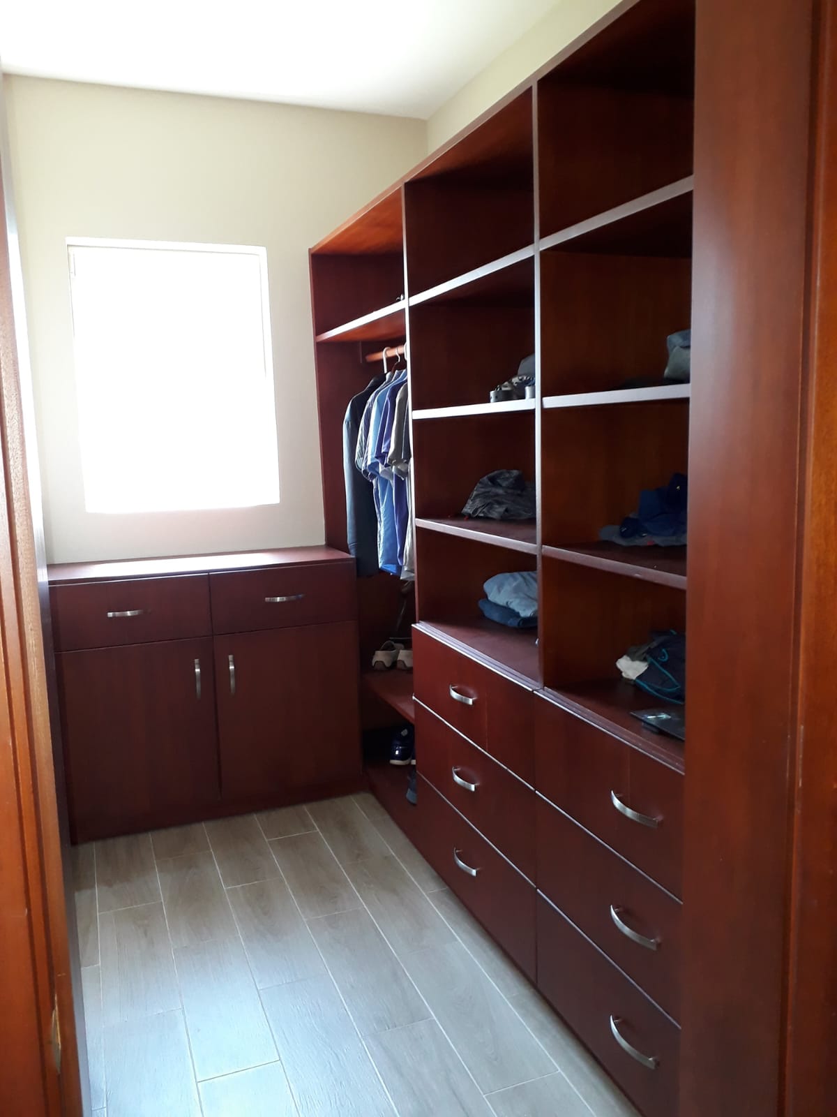 Spacious walk-in closet with dark wood shelving and drawers, organized clothing and shoes.