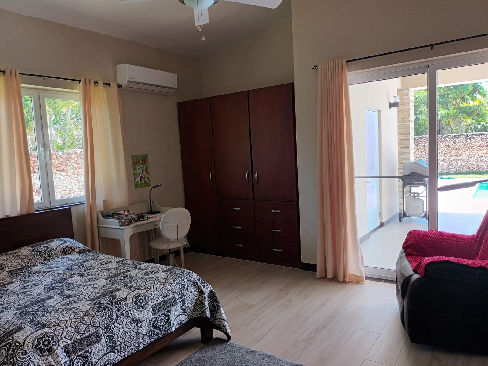 Bedroom with a large wardrobe, desk, bed, and patio doors leading to a pool area.