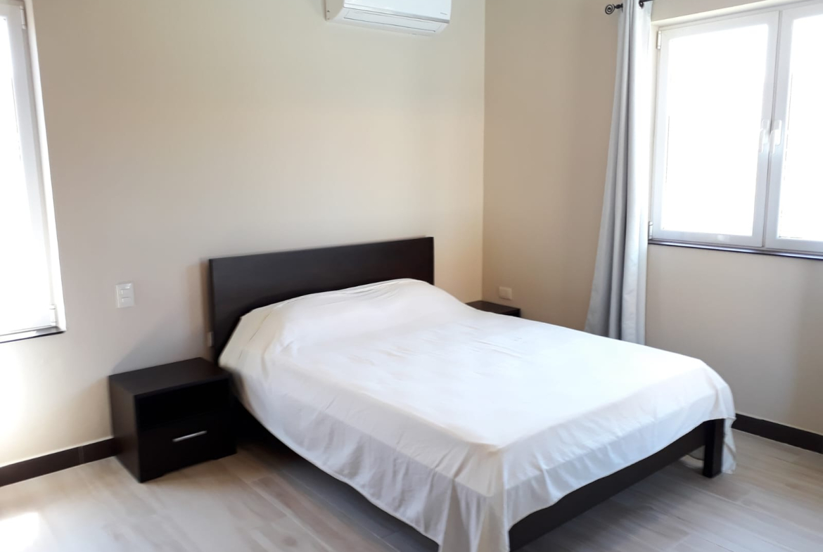 Clean, white-sheeted bed in a minimalist bedroom with air conditioning