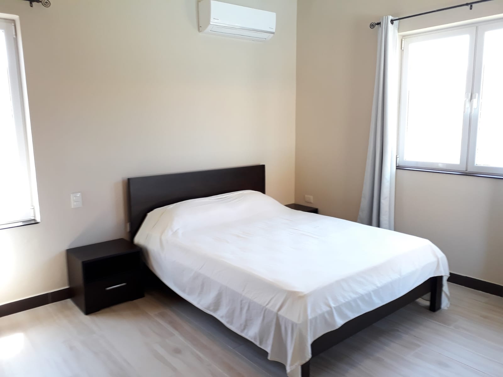 Clean, white-sheeted bed in a minimalist bedroom with air conditioning