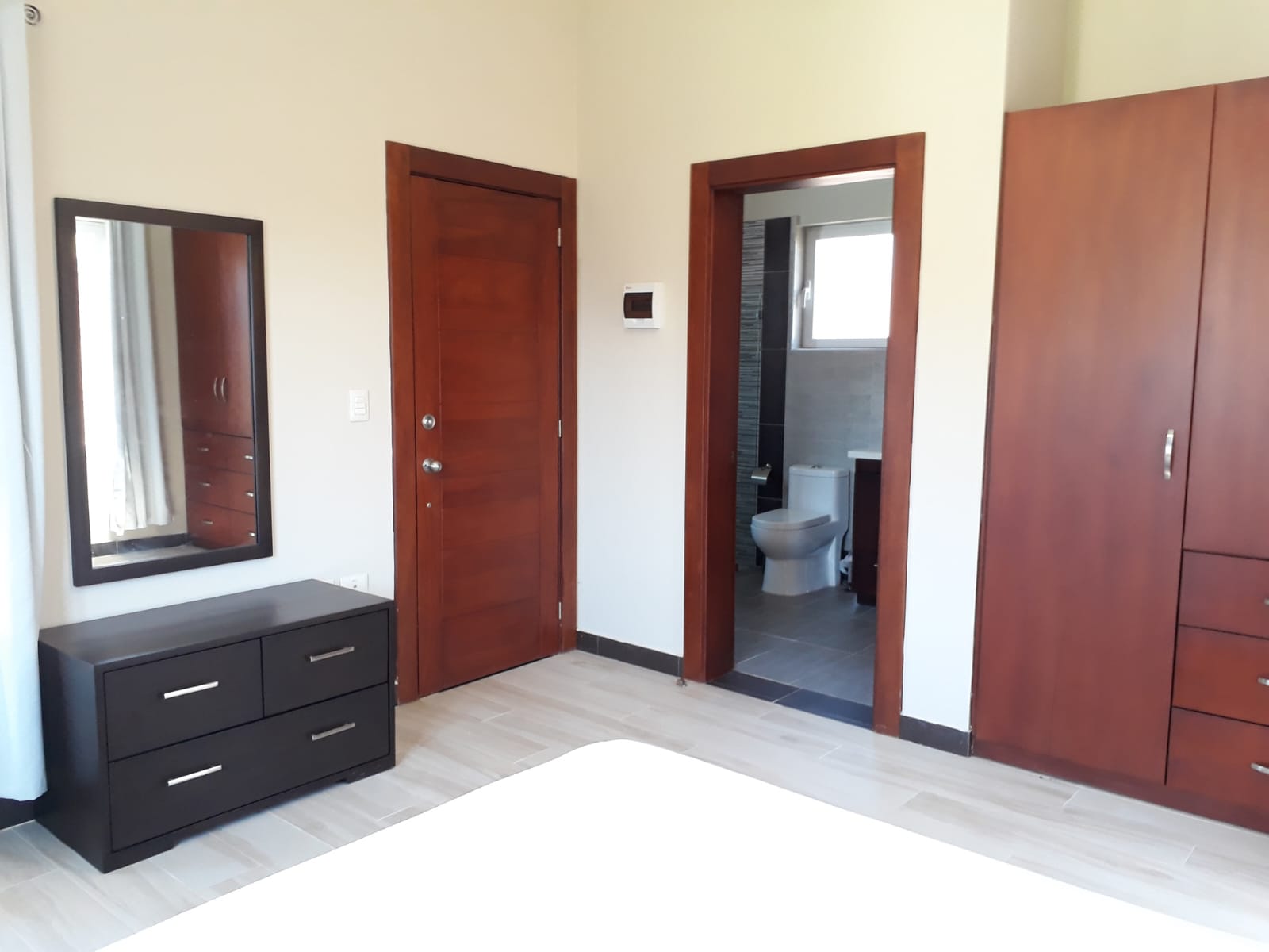 Bedroom with dark dresser, mirror, wooden doors, and ensuite bathroom view.