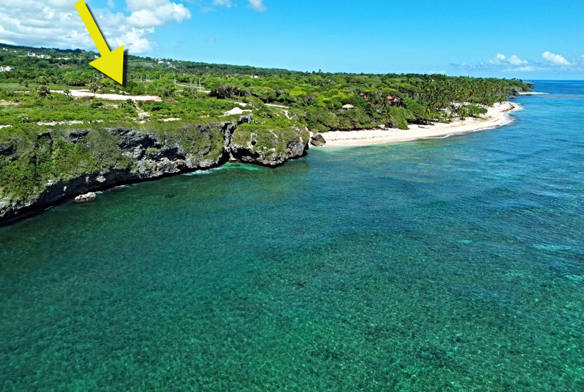 Yellow arrow pointing to a cliffside property overlooking a turquoise ocean and beach.