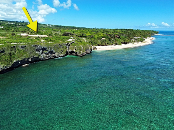 Yellow arrow pointing to a cliffside property overlooking a turquoise ocean and beach.