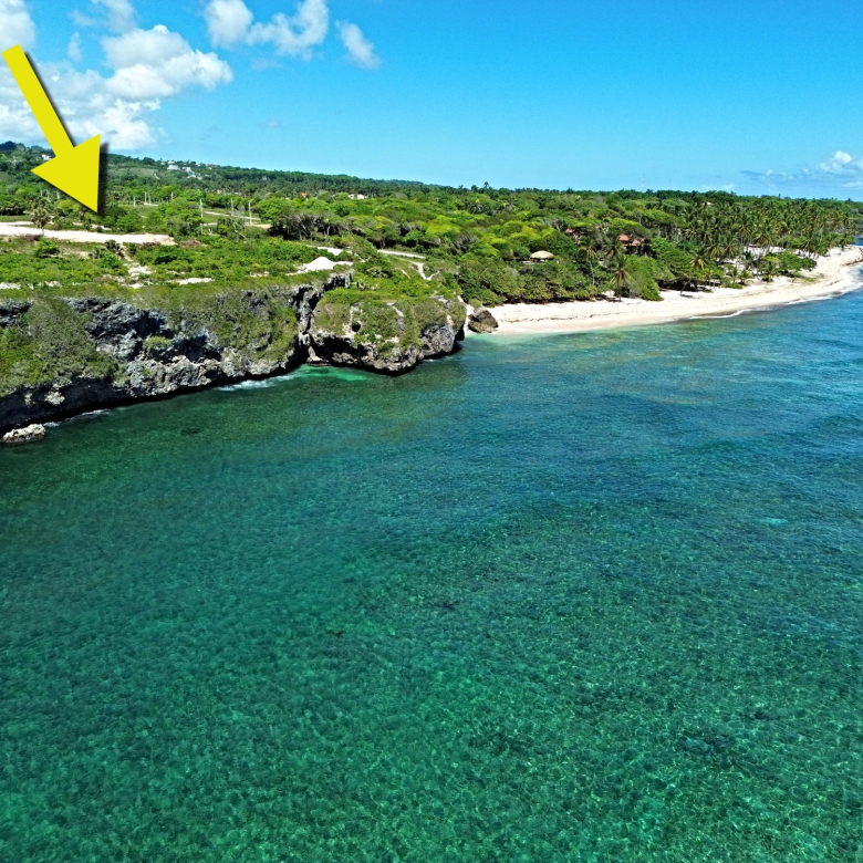 Yellow arrow pointing to a cliffside property overlooking a turquoise ocean and beach.