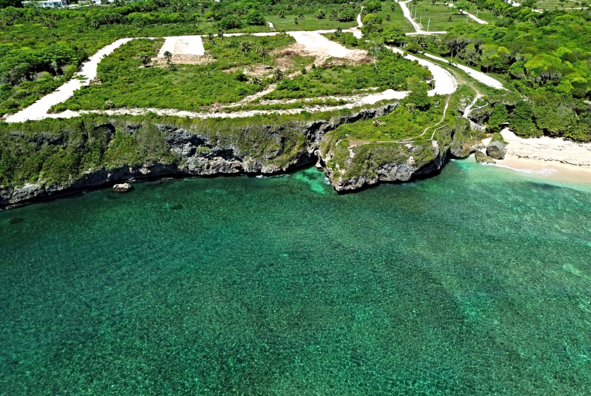 Aerial view of a coastal cliff with a small airstrip and lush green vegetation overlooking turquoise waters and a sandy beach.