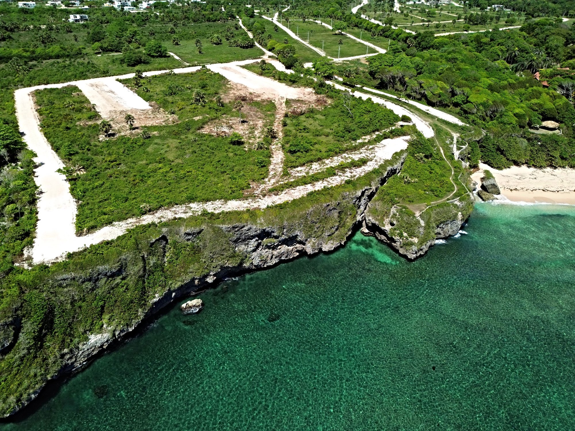 Aerial view of coastal land development with clear turquoise water and lush green cliffs.