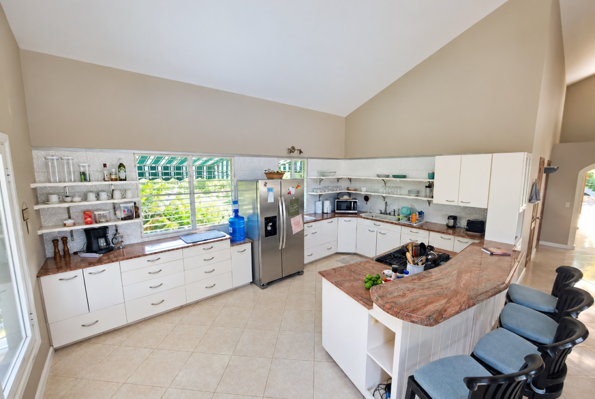 Spacious modern kitchen with white cabinets, granite island, and large windows overlooking greenery