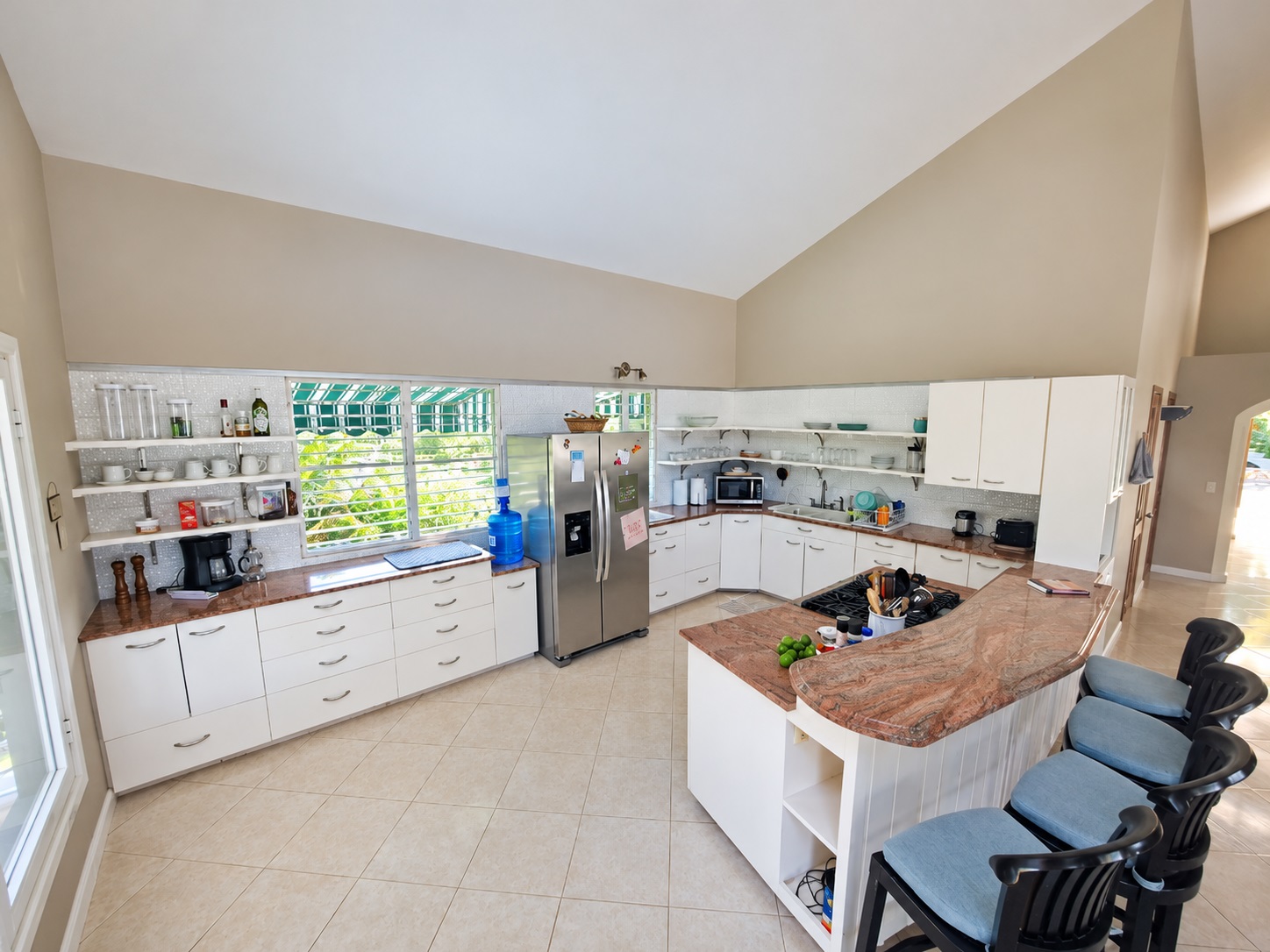 Spacious modern kitchen with white cabinets, granite island, and large windows overlooking greenery