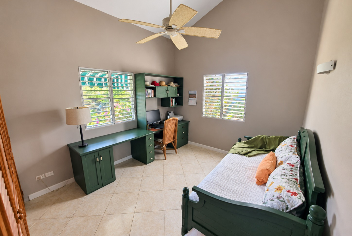 Green desk with computer and chair, daybed with pillows, and ceiling fan in a bright room