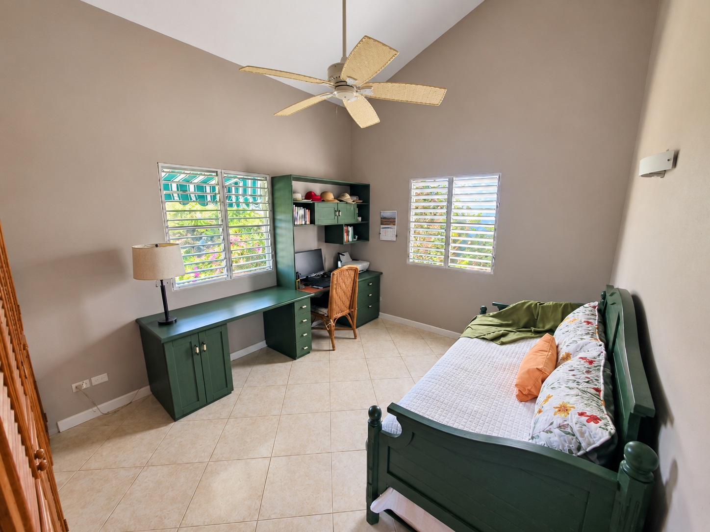 Green desk with computer and chair, daybed with pillows, and ceiling fan in a bright room