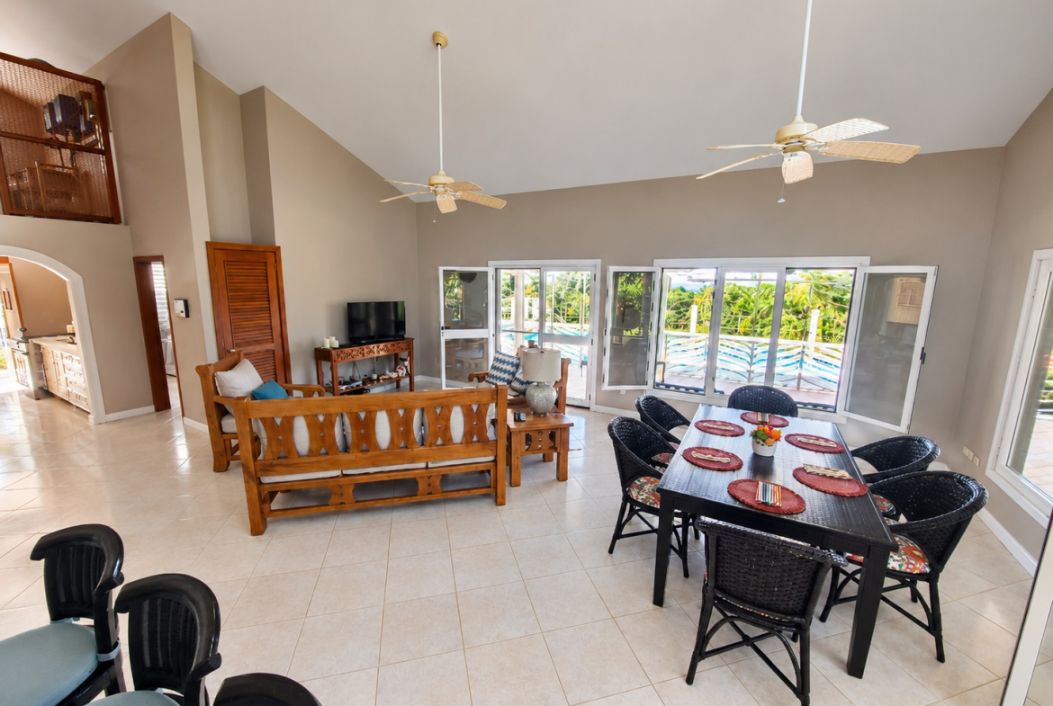 Spacious living and dining area with a pool view, featuring wood furniture and ceiling fans.
