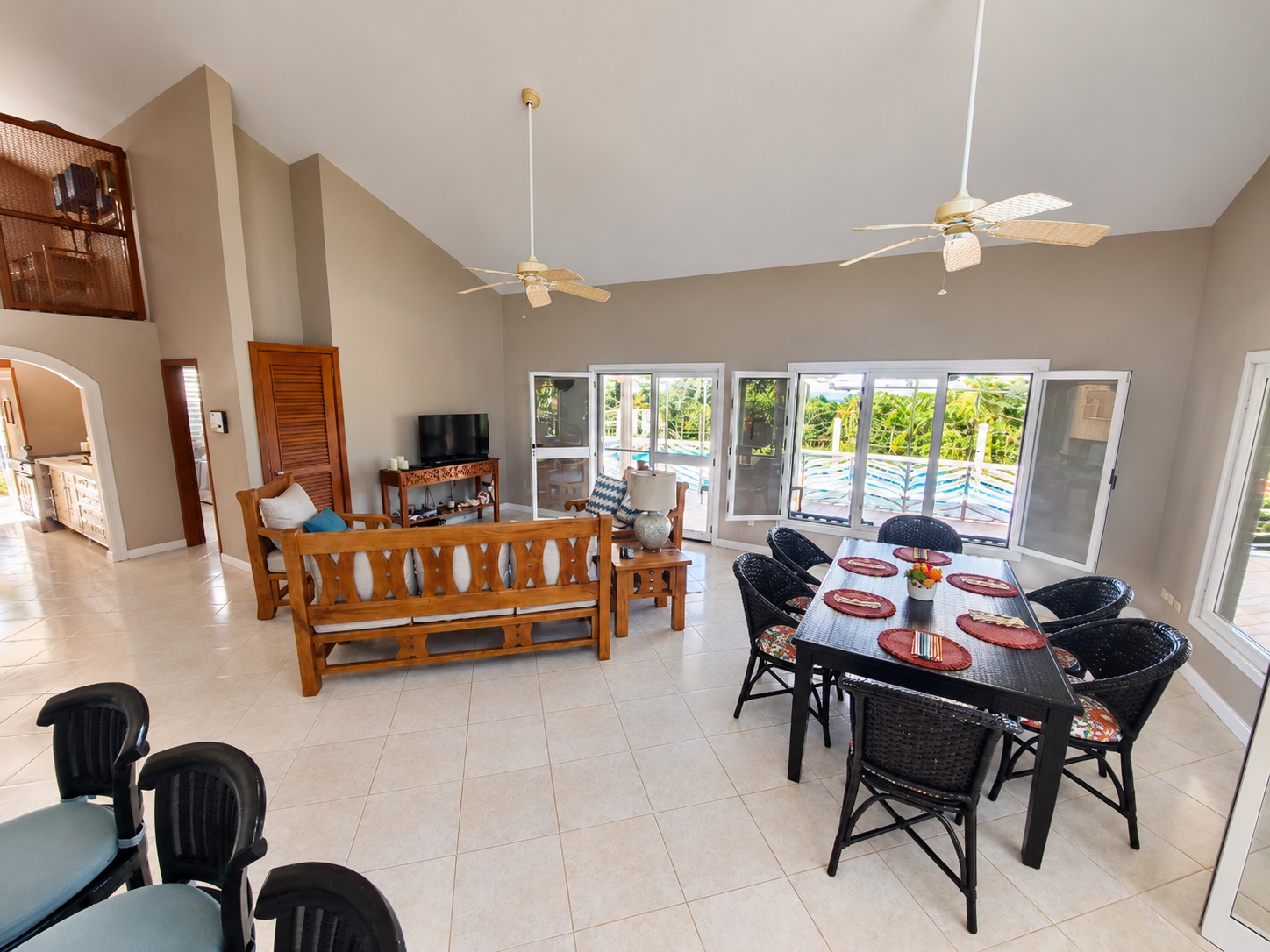 Spacious living and dining area with a pool view, featuring wood furniture and ceiling fans.