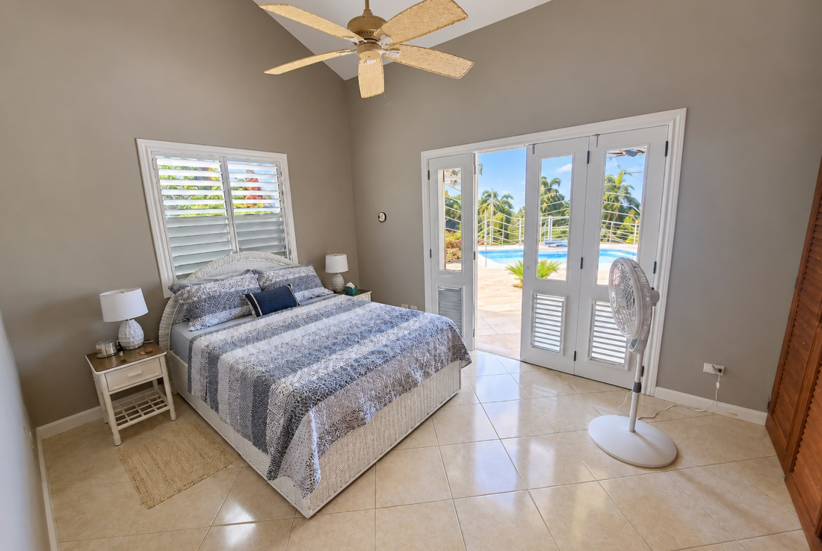 Bedroom with king-size bed, ceiling fan, and patio doors opening to a pool.