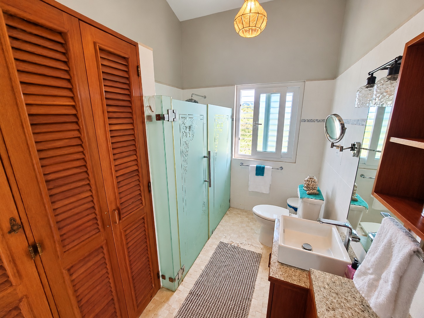 Bright, spacious bathroom with wood cabinets, teal shower doors, and sink